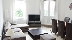 A modern living room with a sofa, a coffee table, a TV, and a dining area with chairs. - Amazing Apartment Antwerp South (Antwerp)