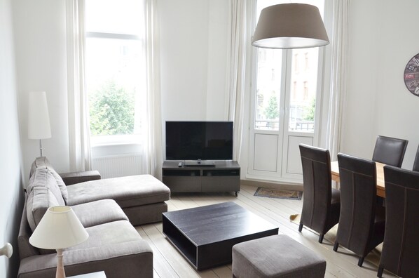 A modern living room with a sofa, a coffee table, a TV, and a dining area with chairs.