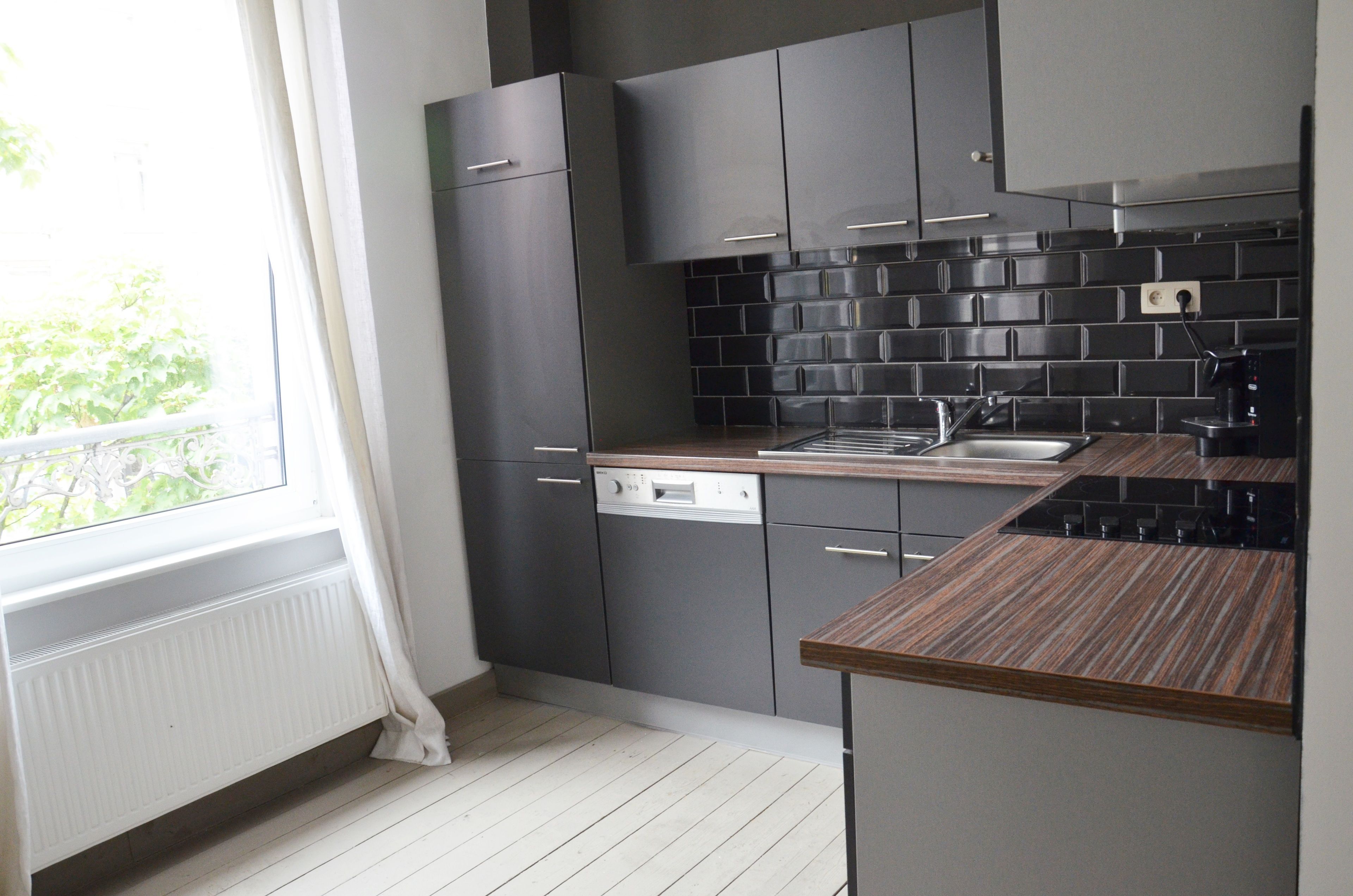 A modern kitchen with grey cabinets, a black tiled backsplash, and a wooden countertop.