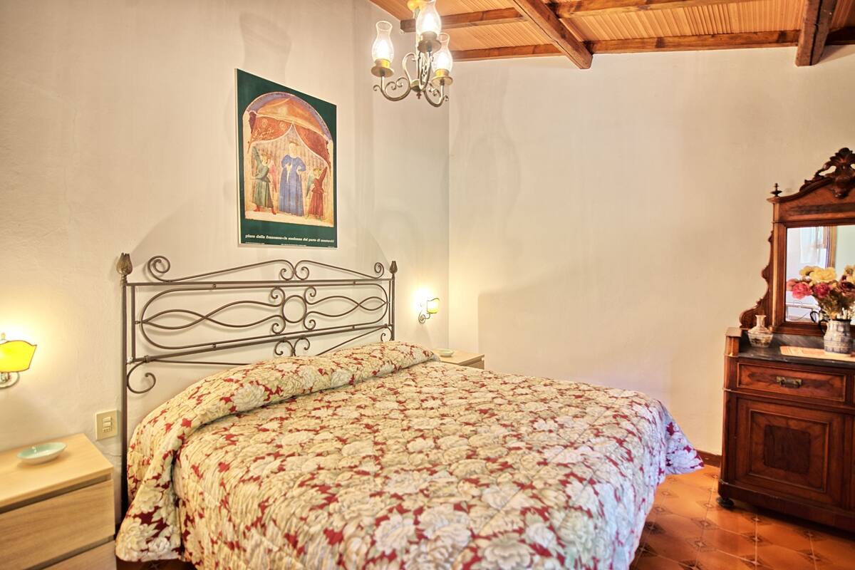 A bedroom with a bed, a nightstand, a dresser, a wall-mounted painting, and a chandelier.