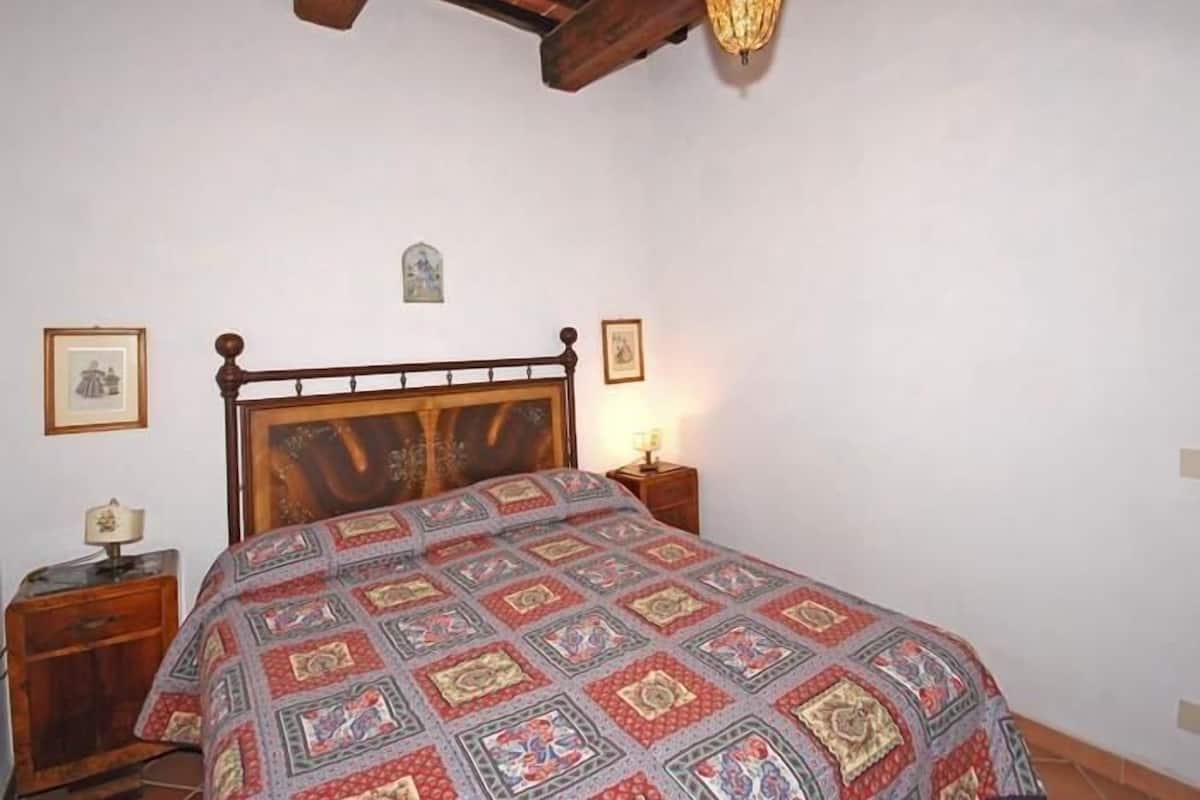 A bedroom with a wooden bed, a nightstand with a lamp, and a small wall decoration.