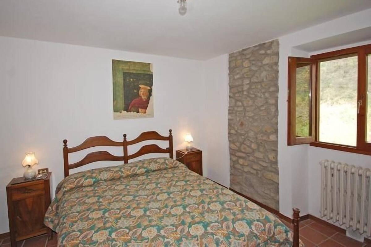 A bedroom with a wooden bed, a stone wall, a window, and a radiator.