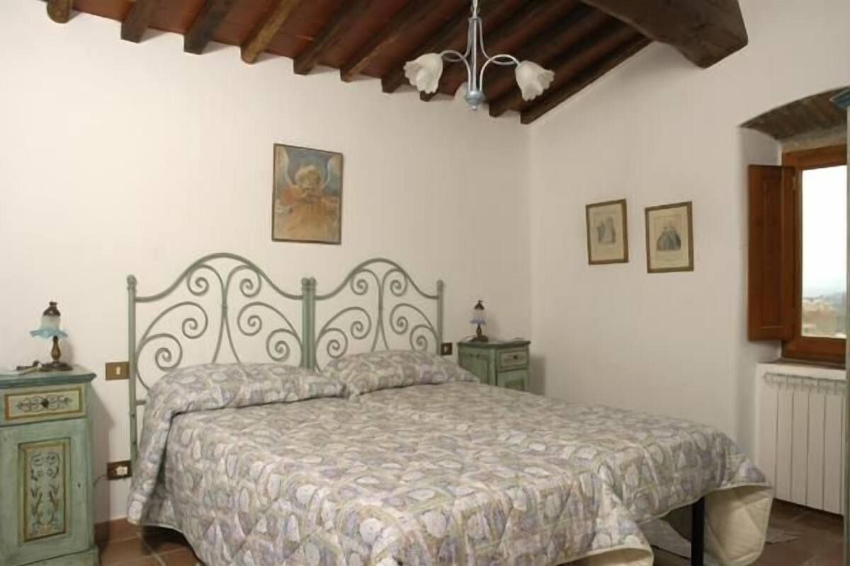 A bedroom with a bed, a nightstand, a dresser, a chandelier, and a window.