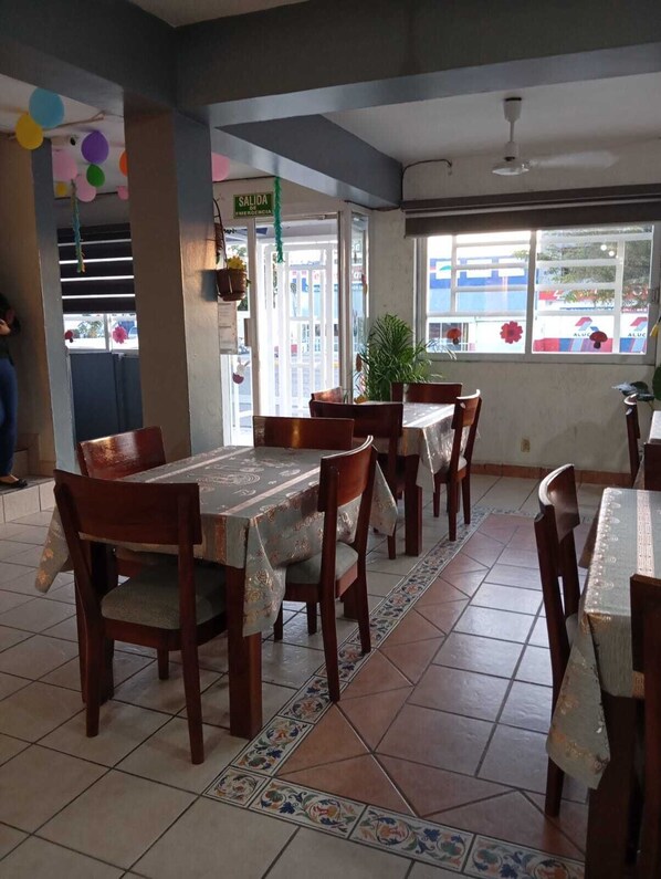 A restaurant with wooden tables and chairs, a tiled floor, and a view of the street through large windows.