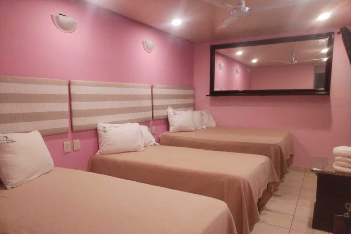 Habitación de hotel con tres camas, un espejo grande y un ventilador de techo.