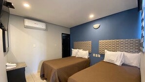 A hotel room with two beds, a small desk, a mirror, and an air conditioning unit. - Hotel Esperanza (Mazatlán)
