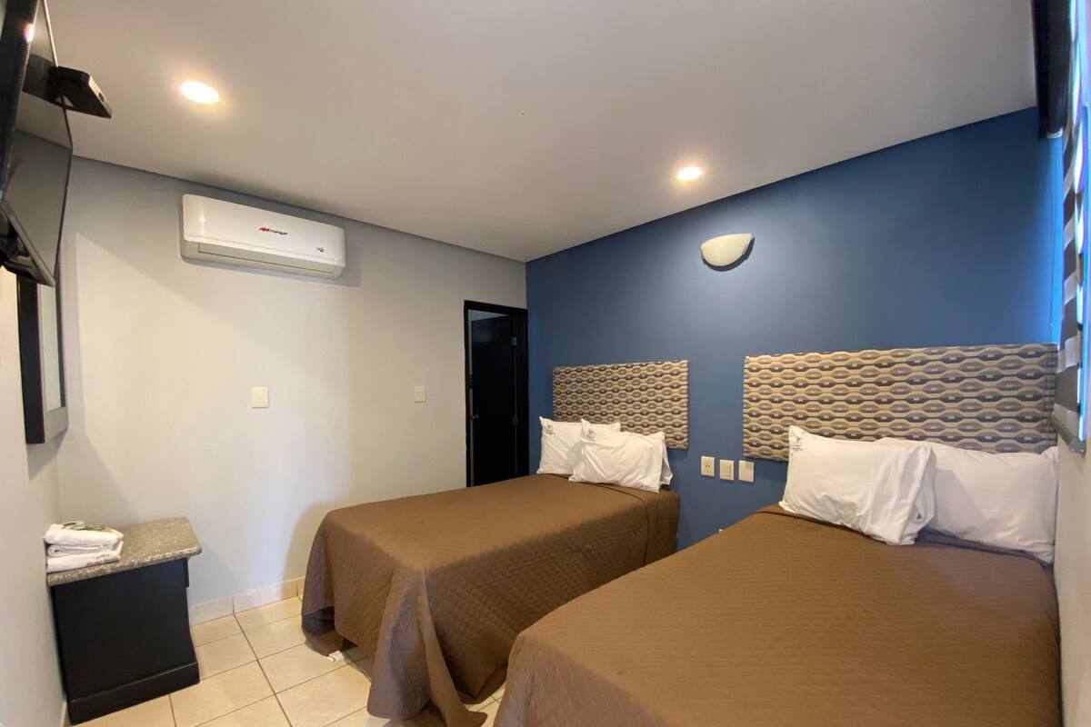 Habitación de hotel con dos camas, un escritorio pequeño, un espejo y un aire acondicionado.