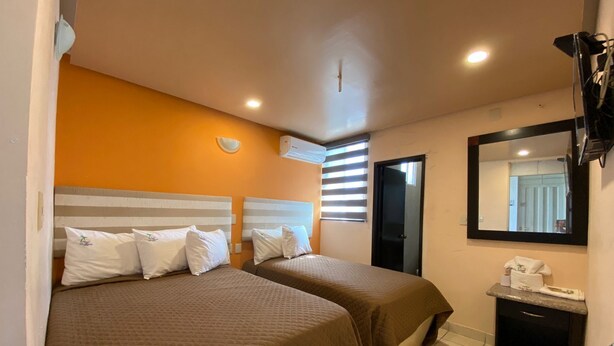 A hotel room with two beds, a small bedside table, a mirror, and a window with blinds. - Hotel Esperanza (Mazatlán)