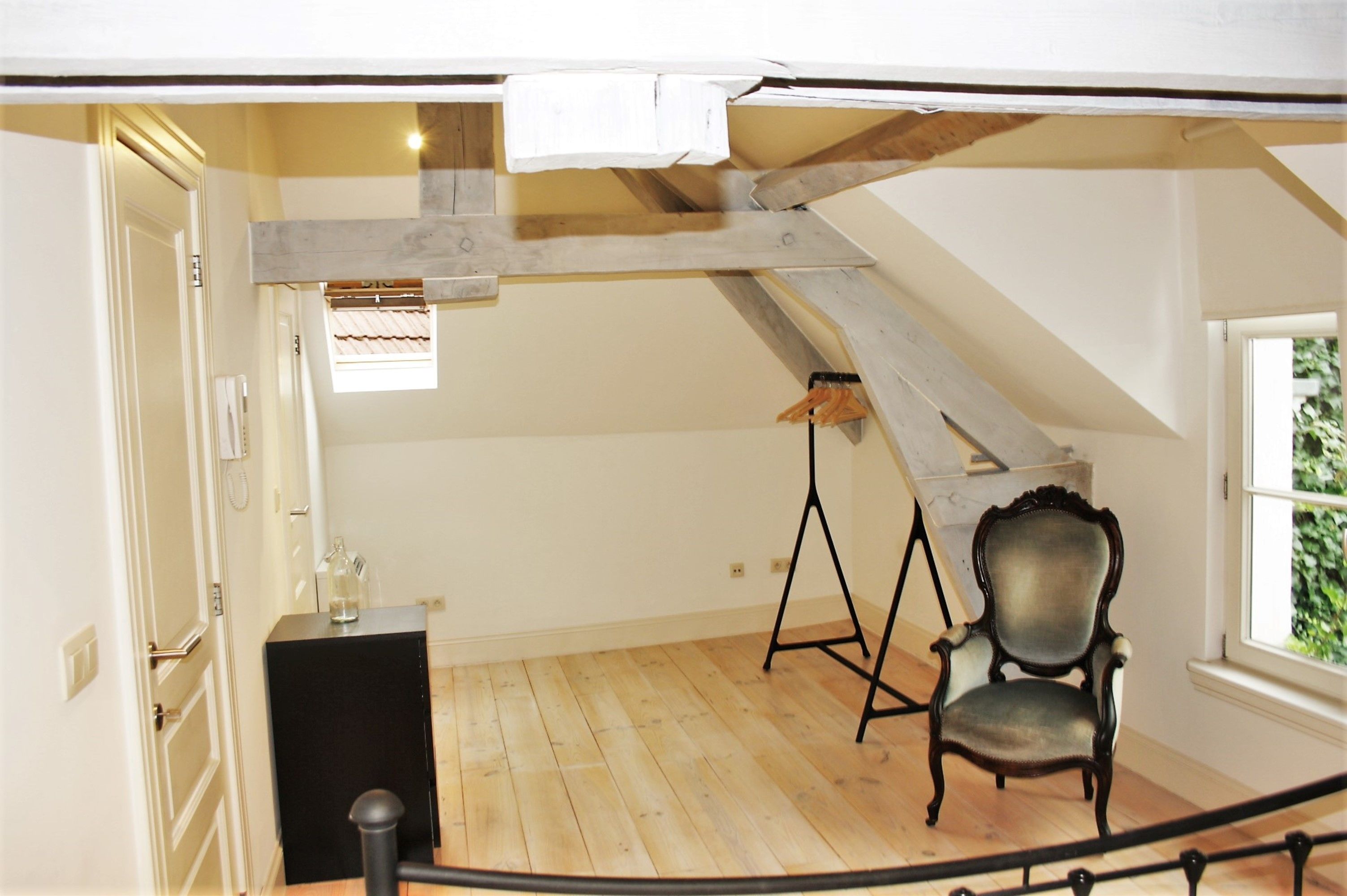 A room with a sloped ceiling, a wooden floor, a chair, a small table, and a window.