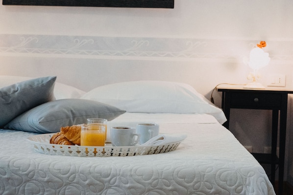 A neatly made bed with a tray of breakfast items including croissants, orange juice, and coffee cups.