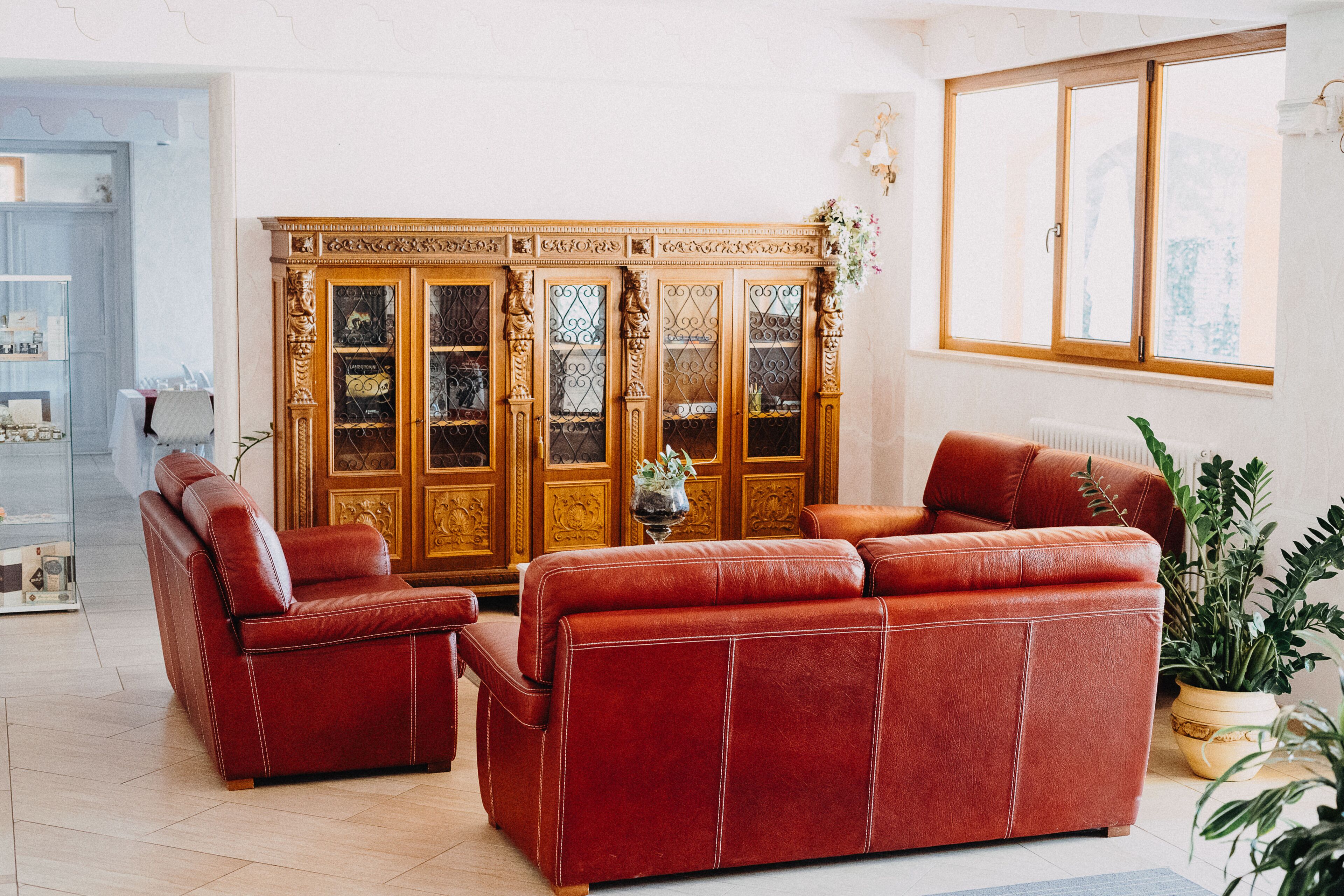 A living room with a red leather sofa set, a wooden cabinet with glass doors, and a large window with a view of greenery.