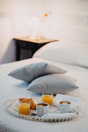 A breakfast tray on a bed with croissants, orange juice, and coffee cups.