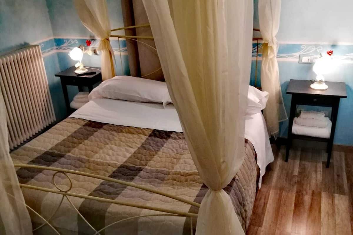 Makuuhuone, jossa on sänky, yöpöytä lampun kanssa, patteri ja verho.