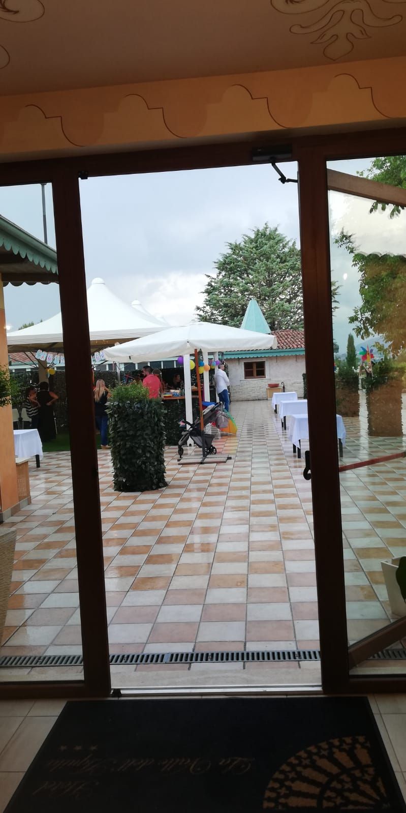 Ένας εξωτερικός χώρος με πλακόστρωτο δάπεδο, μια λευκή τέντα και ένα μικρό κτίριο με κεραμοσκεπή.