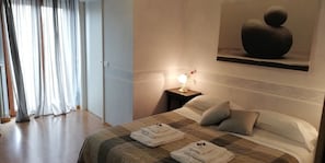 A hotel room with a bed, pillows, a bedside table with a lamp, and a painting on the wall.