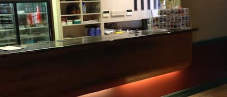 A hotel reception area with a counter, shelves with various items, and a refrigerator.