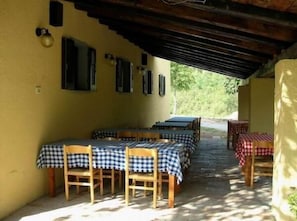 An outdoor patio area with tables and chairs, covered by a wooden roof, and surrounded by yellow walls. - Agriturismo Orsaiola (Urbania)