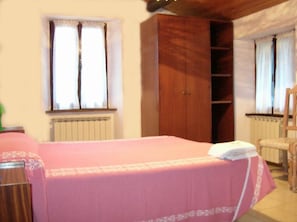 A bedroom with a bed, wooden wardrobe, and two windows with curtains. - Agriturismo Orsaiola (Urbania)