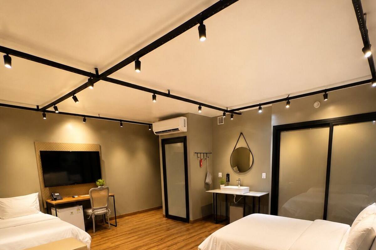 A hotel room with two beds, a desk, a TV, a mirror, and a shower.