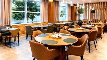 A restaurant with round tables, cushioned chairs, and pendant lighting.