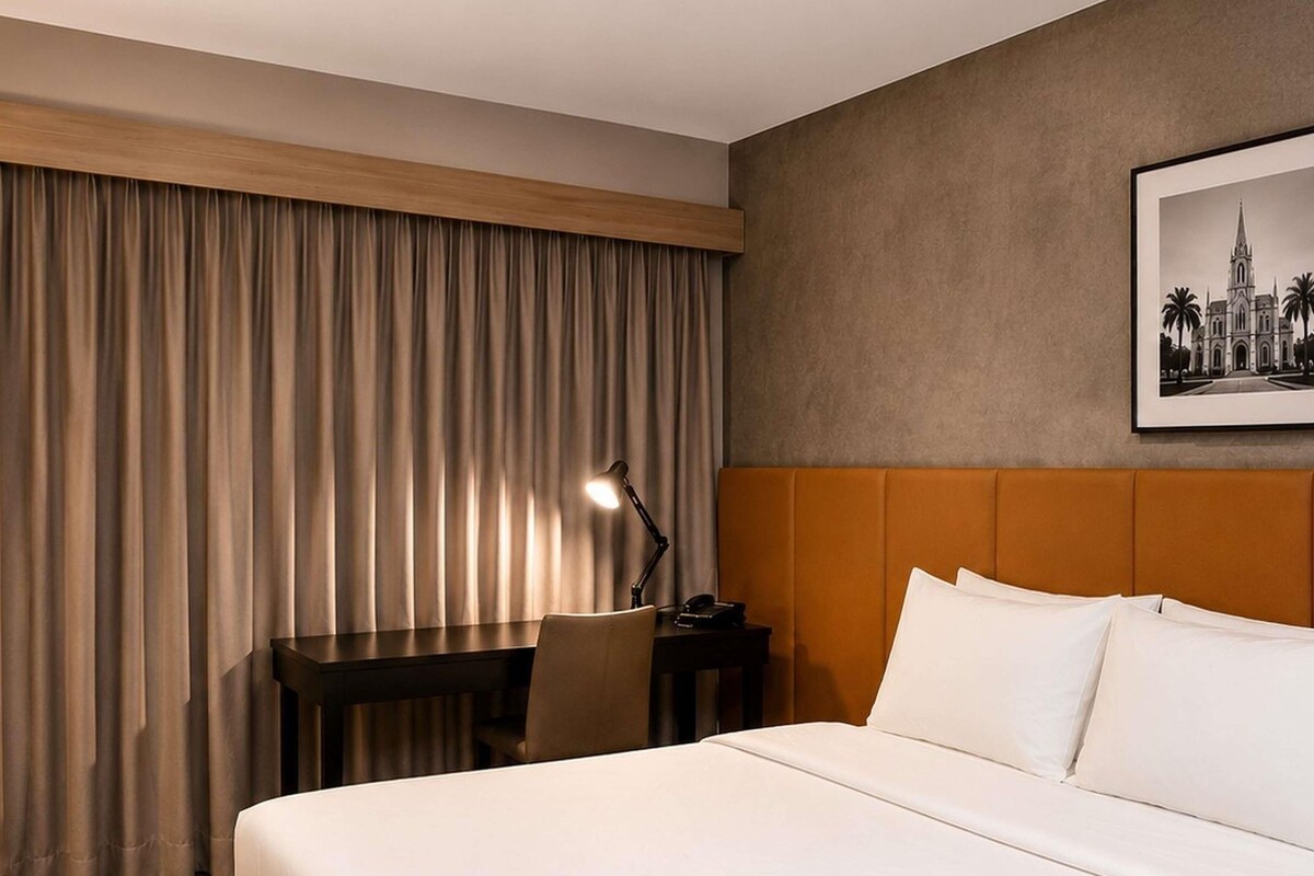 A hotel room with a large bed, a desk with a lamp, and a framed picture on the wall.