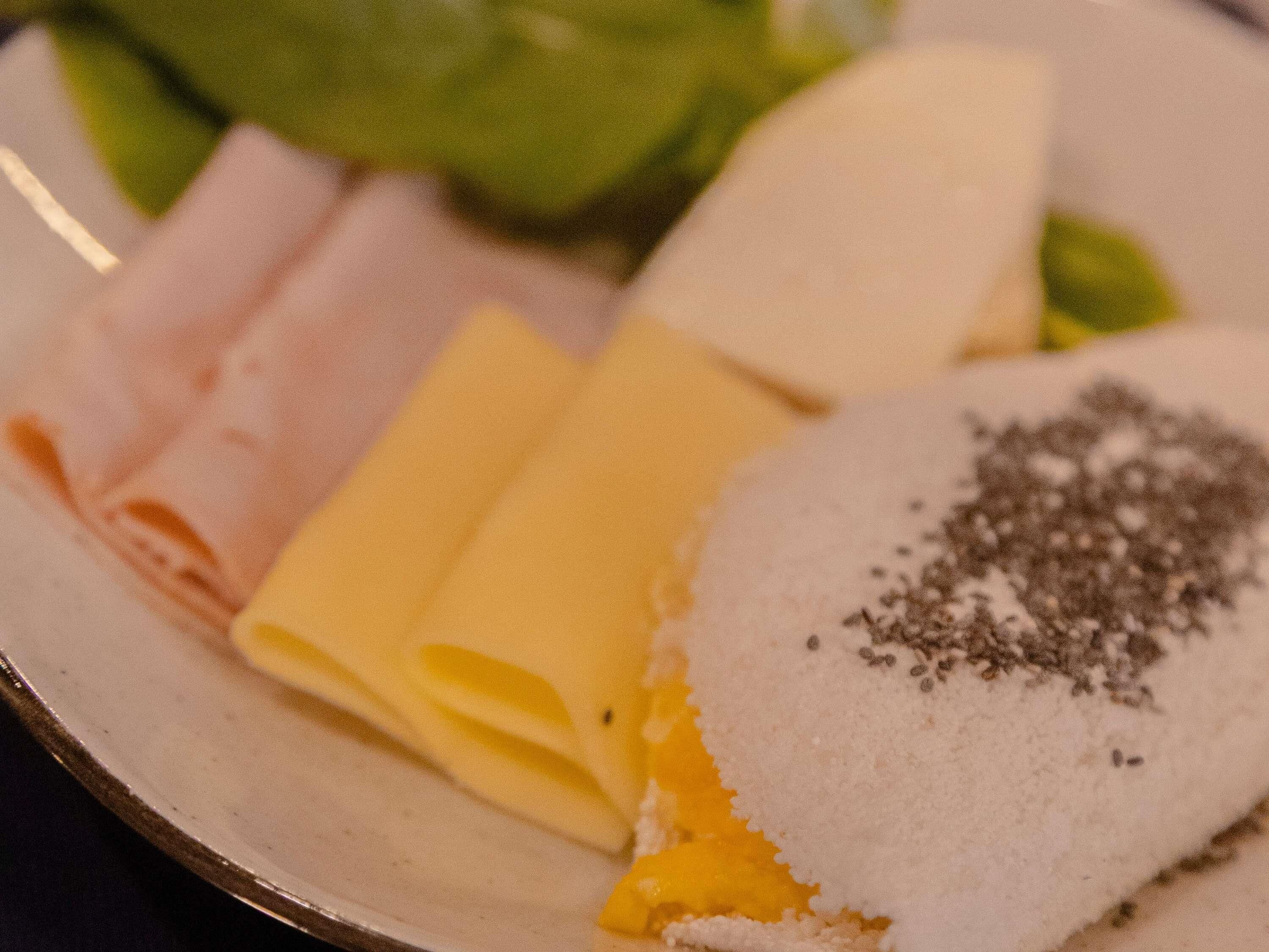 A plate with slices of ham, cheese, and a bread roll with seeds.