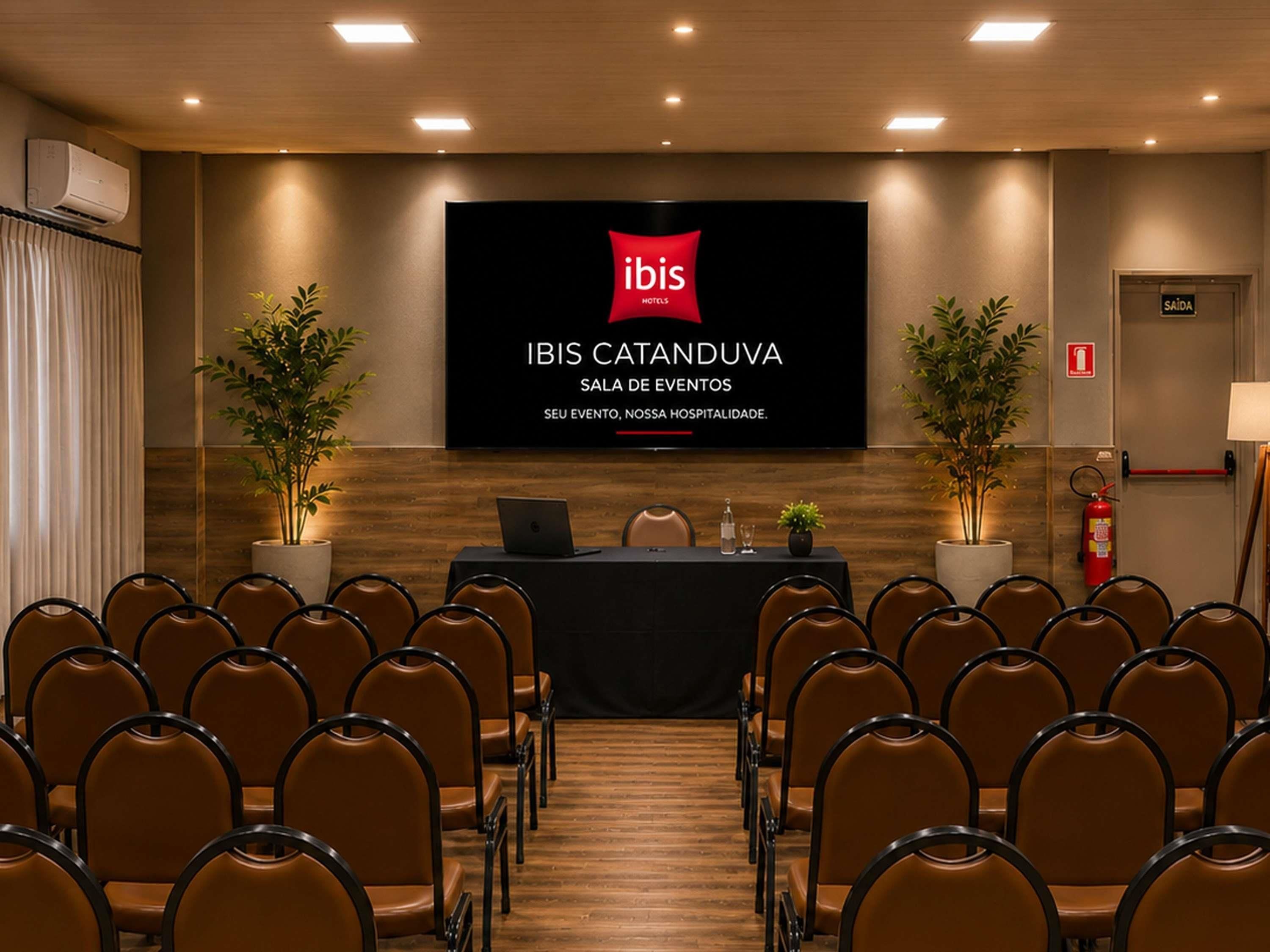 A conference room with a stage, chairs, and a screen displaying the hotel's name and event hall.