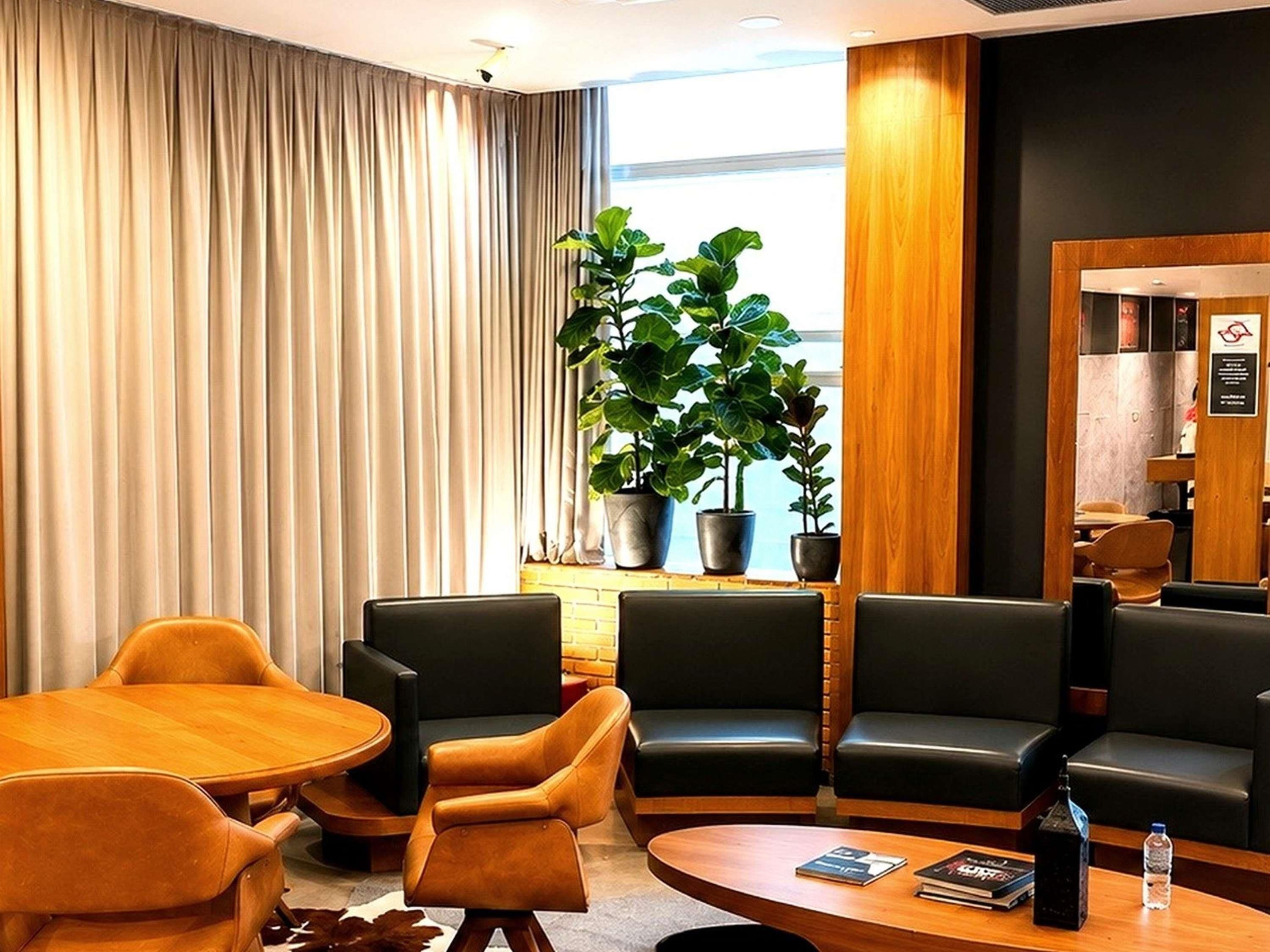 Um saguão de hotel com assentos de couro, uma mesa de centro de madeira e uma janela grande com cortinas.