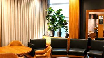 Um saguão de hotel com assentos de couro, uma mesa de centro de madeira e uma janela grande com cortinas.