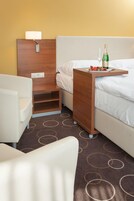 A hotel room with a bed, a bedside table with a bottle of champagne and a glass, a lamp, and a chair.