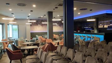 Un intérieur de restaurant moderne avec plusieurs espaces de restauration, comprenant des tables et des chaises, ainsi qu’un bar doté d’un comptoir éclairé en bleu.