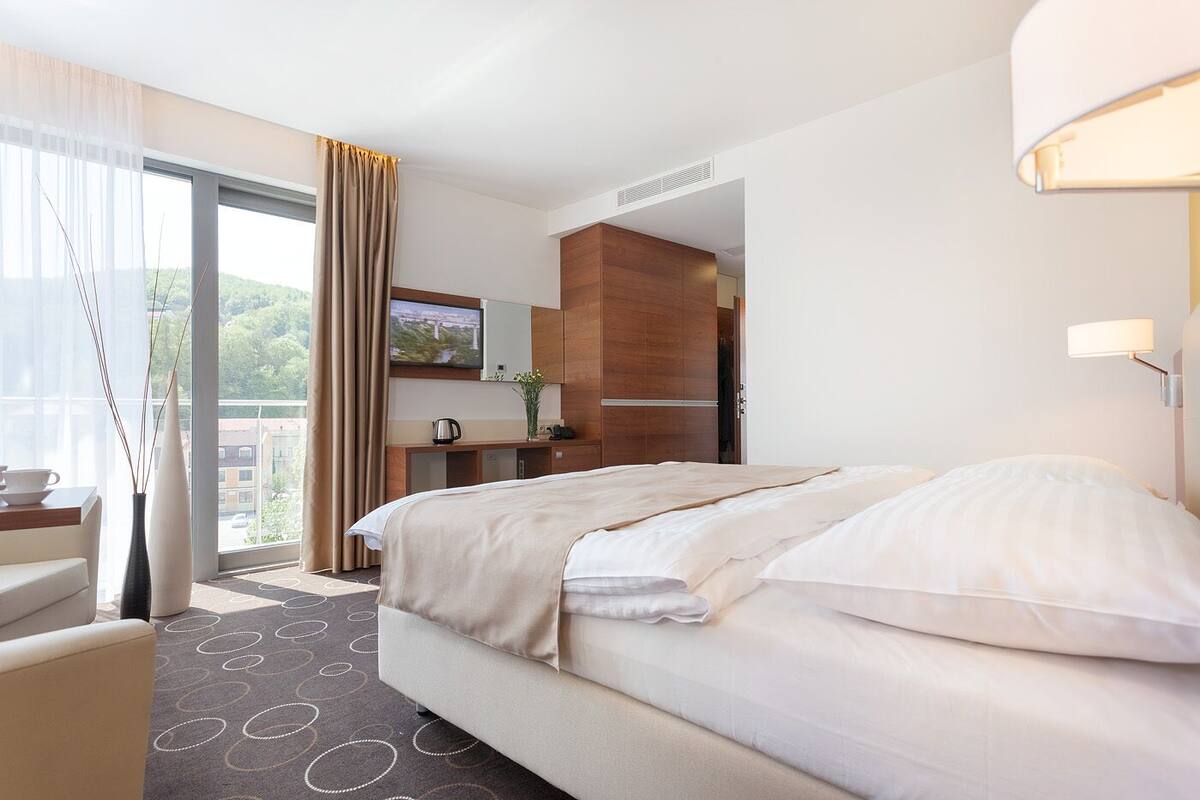 Quarto de hotel com uma cama grande, uma mesa, uma cadeira, uma televisão e vista para o exterior.