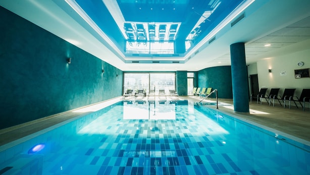 Una piscina interior con suelo de baldosas, luces en el techo y sillones de descanso a lo largo de las paredes.