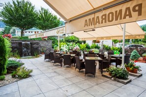 An outdoor patio area with multiple tables and chairs, a waterfall feature, and potted plants. - Hotel Panorama (Trencianske Teplice)