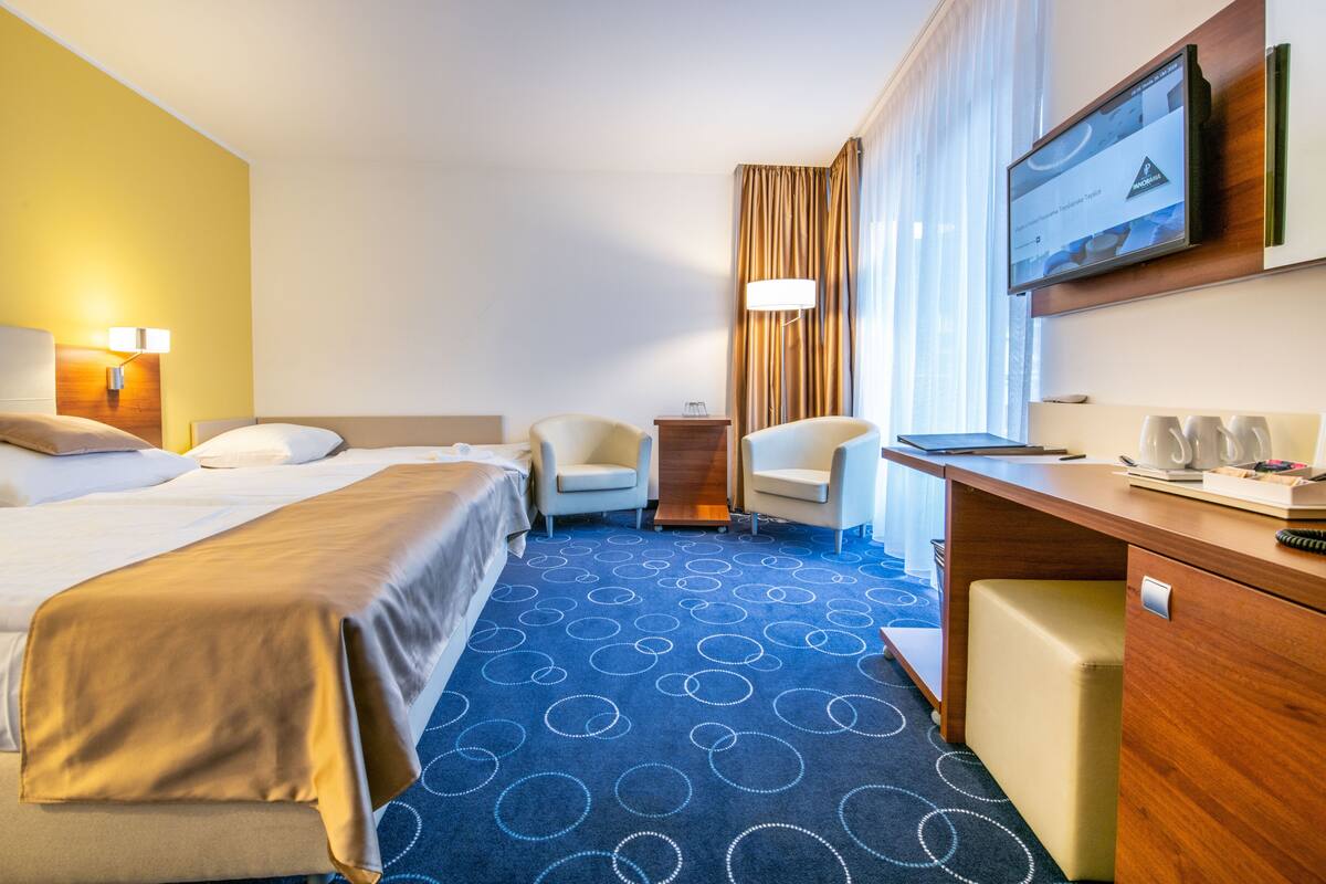 Quarto de hotel com uma cama, duas poltronas, uma escrivaninha e uma televisão.