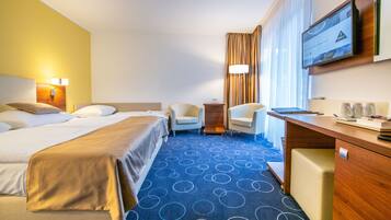 Ein Hotelzimmer mit einem Bett, zwei Sesseln, einem Schreibtisch und einem Fernseher.