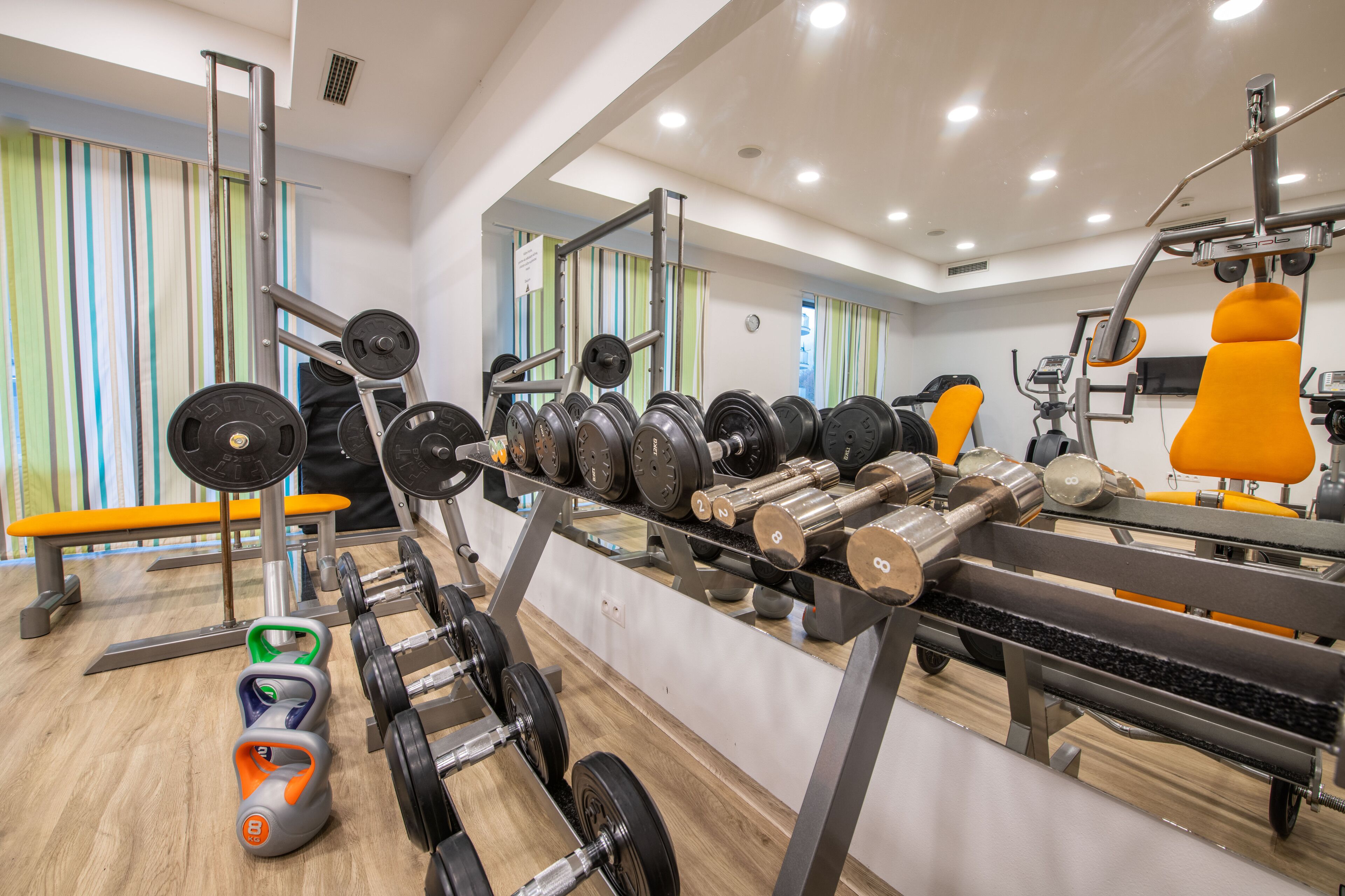 A gym with weightlifting equipment, benches, and a mirror.