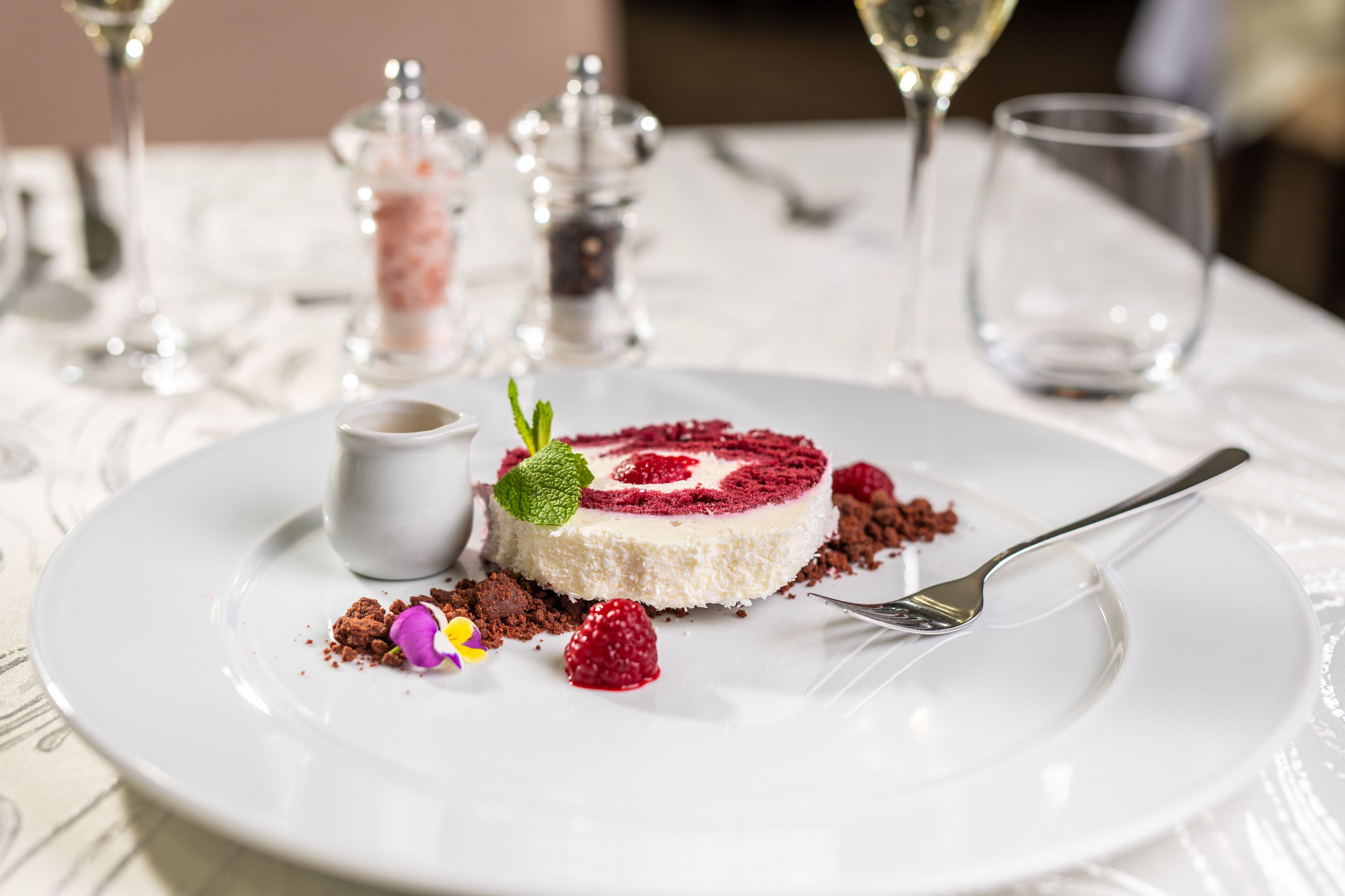 Un postre en un plato blanco con un tenedor, rodeado de migas de chocolate y una hoja de menta.