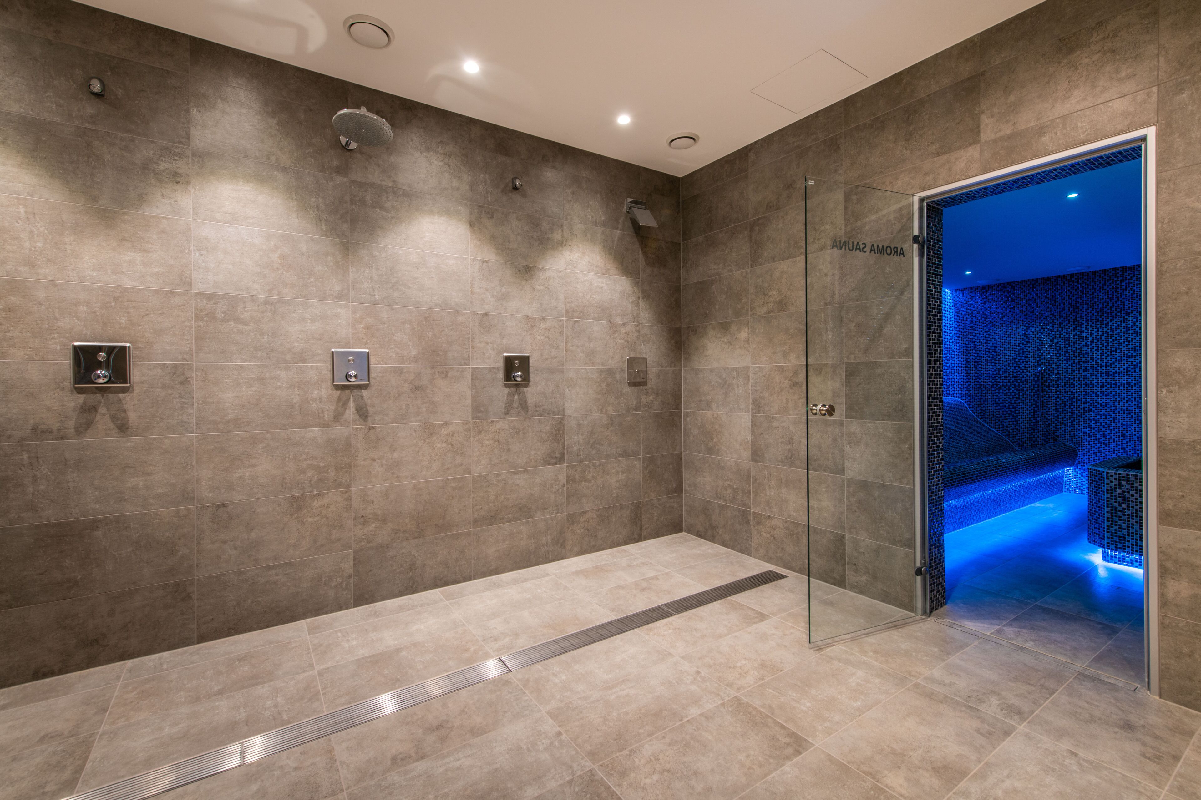 Un baño moderno con cabina de ducha de vidrio, suelo con calefacción y zona de relajación con iluminación azul.