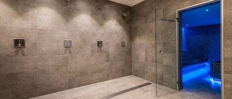 Un baño moderno con cabina de ducha de vidrio, suelo con calefacción y zona de relajación con iluminación azul.