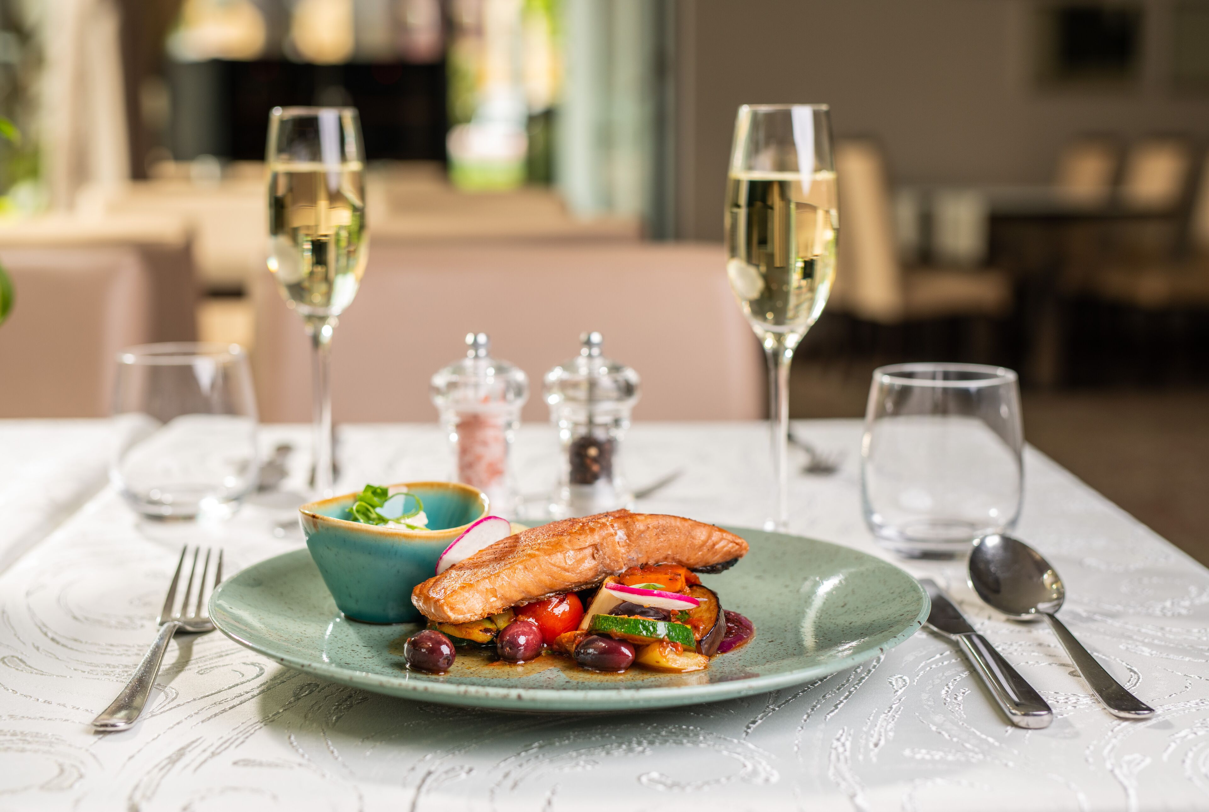 Ein Esstisch mit einem Teller Essen, zwei Gläsern Weißwein und Besteck.