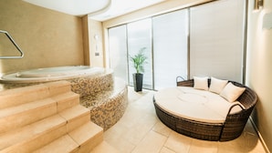 Un área de spa con un jacuzzi, un sofá de mimbre y una escalera que lleva a un balcón.