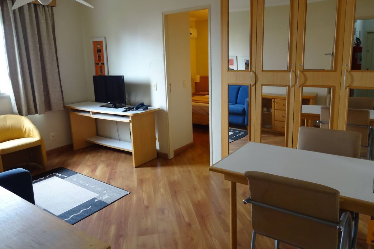 Una habitación con un escritorio de madera, una computadora, una silla, un sofá y una mesa de comedor.