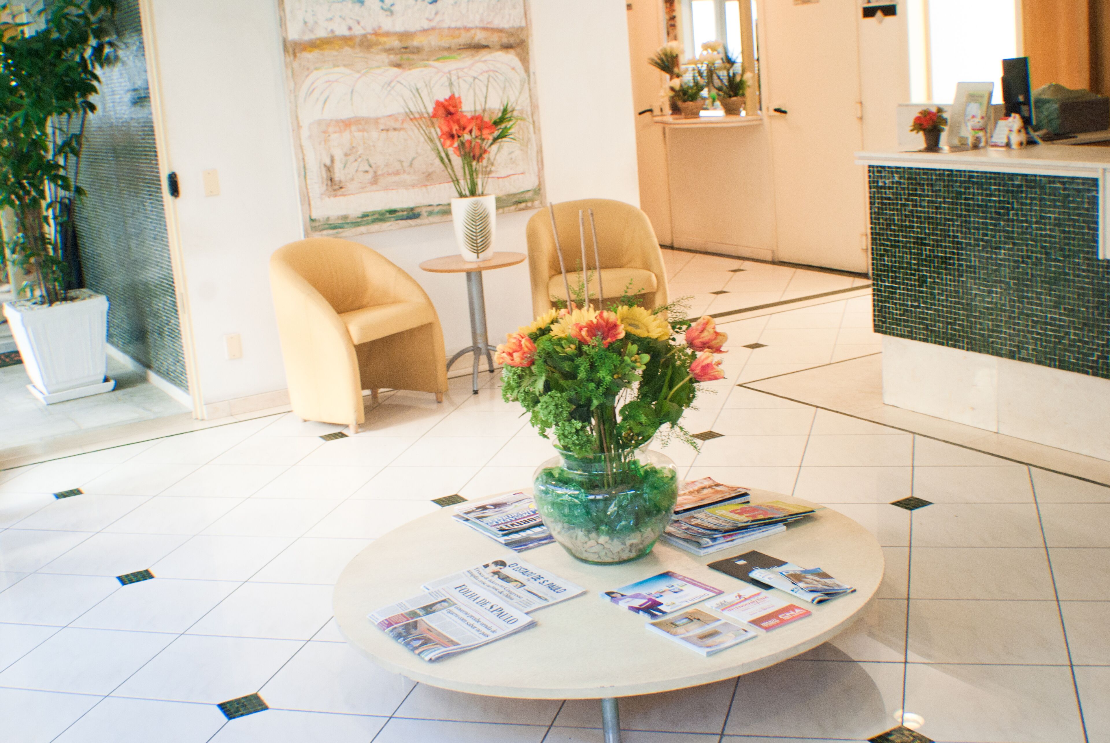 A reception area with a round table displaying magazines, a vase with flowers, and a reception desk.