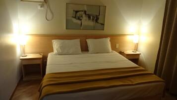 Habitación de hotel con una cama, dos mesitas de noche, un aire acondicionado de pared y un cuadro sobre la cama.