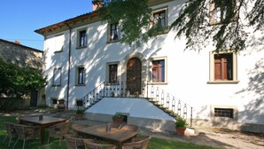 A white building with a stone facade, a wooden staircase, and outdoor furniture. - Villa Capolona (Capolona)