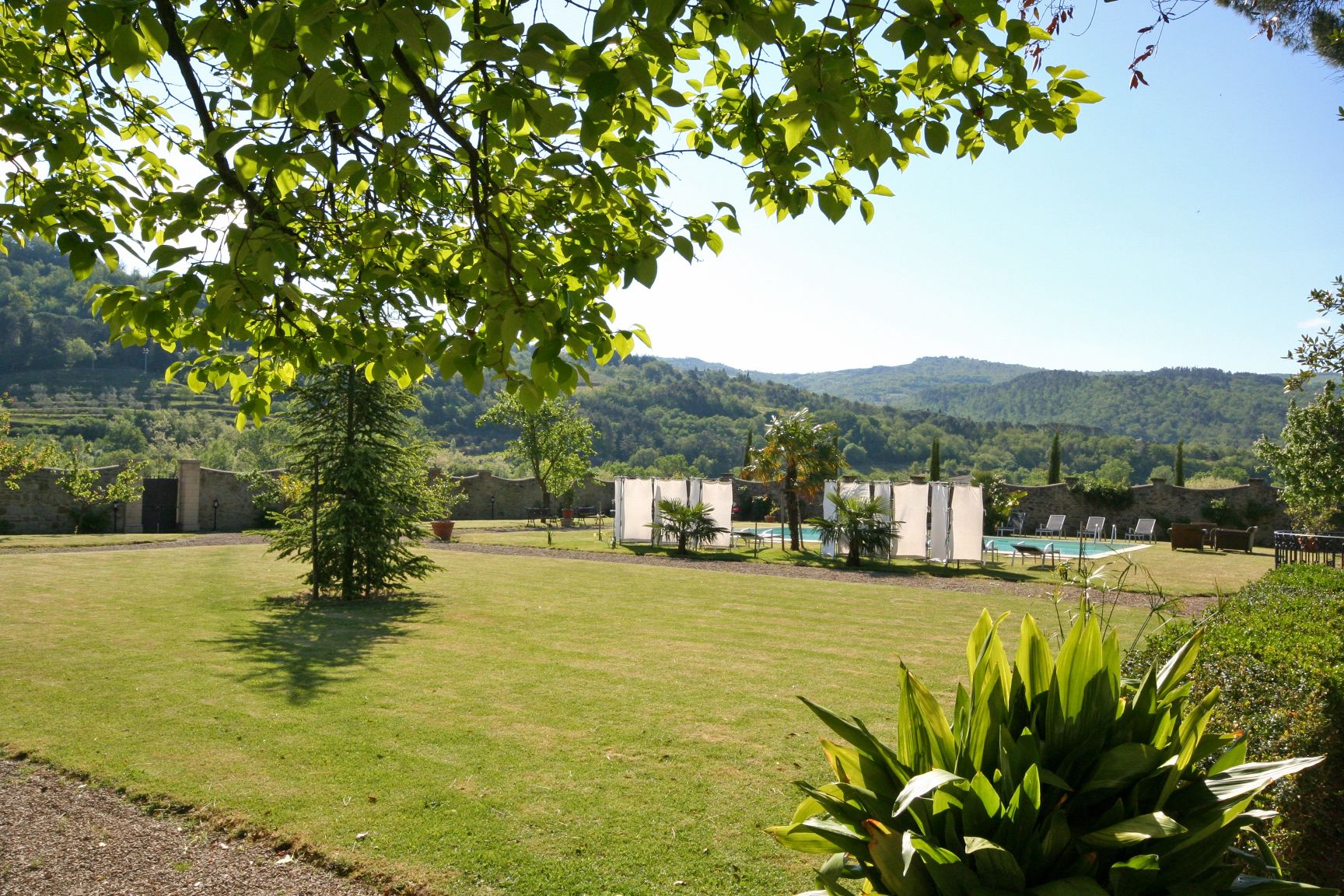 Un espacio al aire libre con césped, una piscina, sillas de descanso y vistas a colinas al fondo.