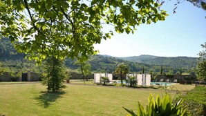 A grassy outdoor area with a pool, lounge chairs, and a view of hills in the background. - Villa Capolona (Capolona)