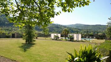 Un espacio al aire libre con césped, una piscina, sillas de descanso y vistas a colinas al fondo.