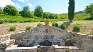 A stone structure with a water feature, surrounded by greenery and trees. - Villa Poggiolino (Subbiano)